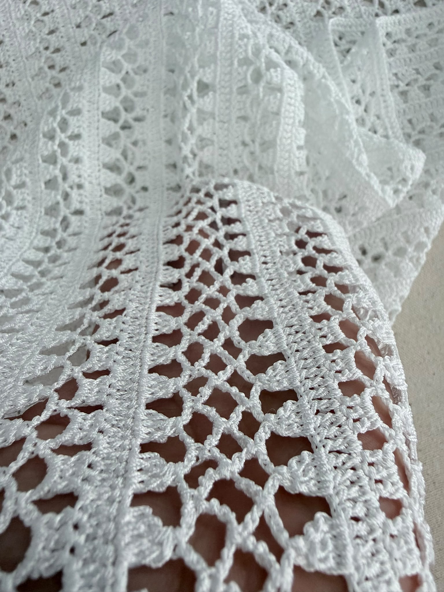 Close-up of the shiny white crochet fabric showing alternating openwork rows and clearly defined stitch texture.