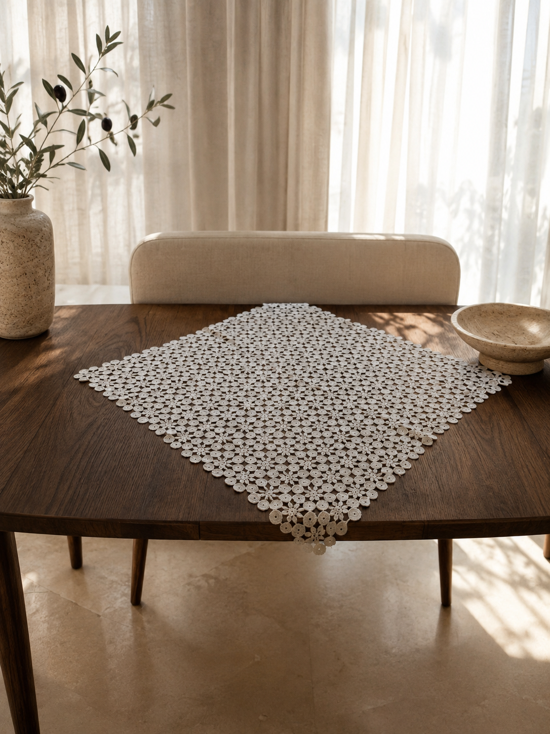 Large white crochet doily displayed diagonally on a dining table, showing its square shape and decorative lace surface.