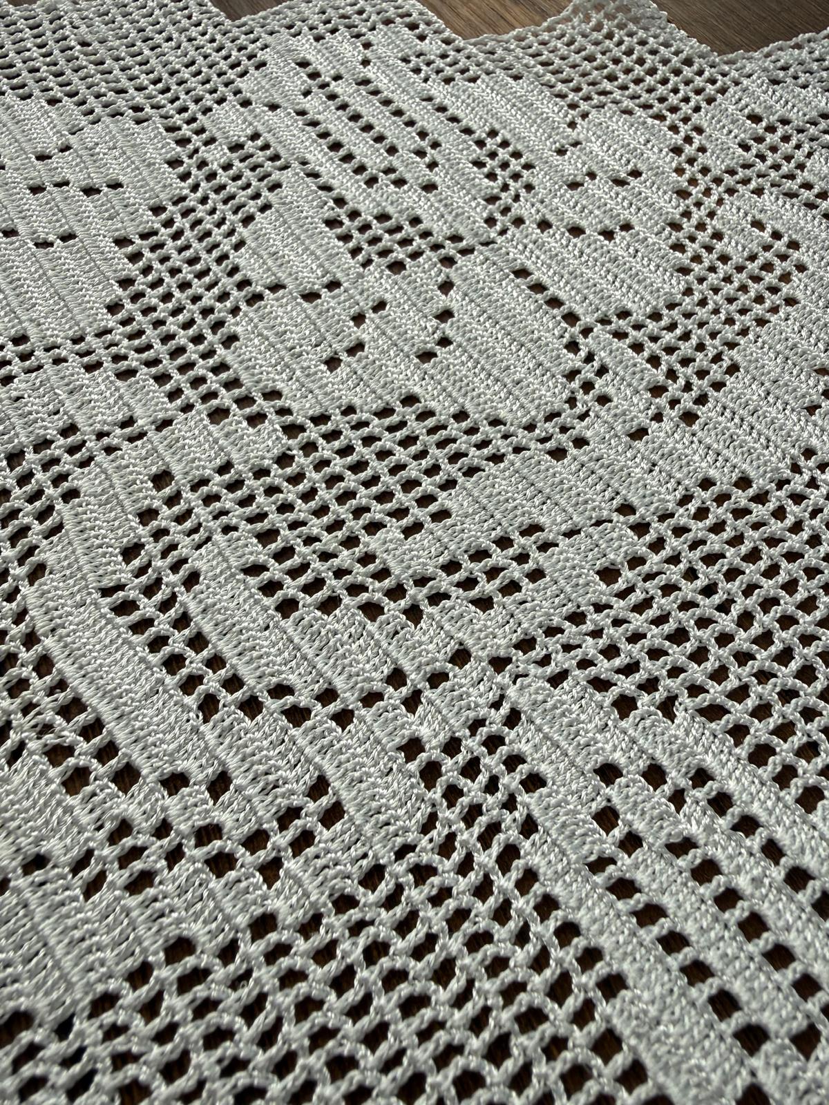 Close-up of the handmade white crochet lace showing the geometric stitch structure and pointed edge detail.