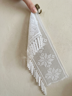 White floral crochet lace panel with fringe held by hand against neutral fabric