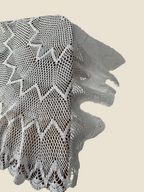 Close-up of the folded scalloped border and layered crochet pattern of the white lace table topper.