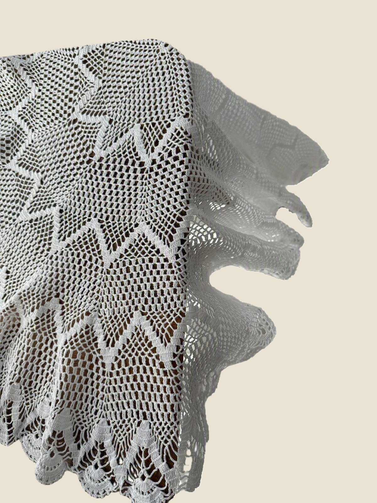 Close-up of the folded scalloped border and layered crochet pattern of the white lace table topper.