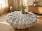 Styled view of the handmade white crochet lace table topper with its softly gathered edge around a round table.