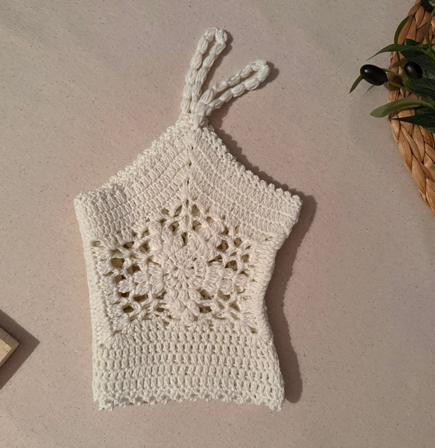 Angled flat-lay view of the white cotton crochet top highlighting the floral motif construction, straps and open lacework.