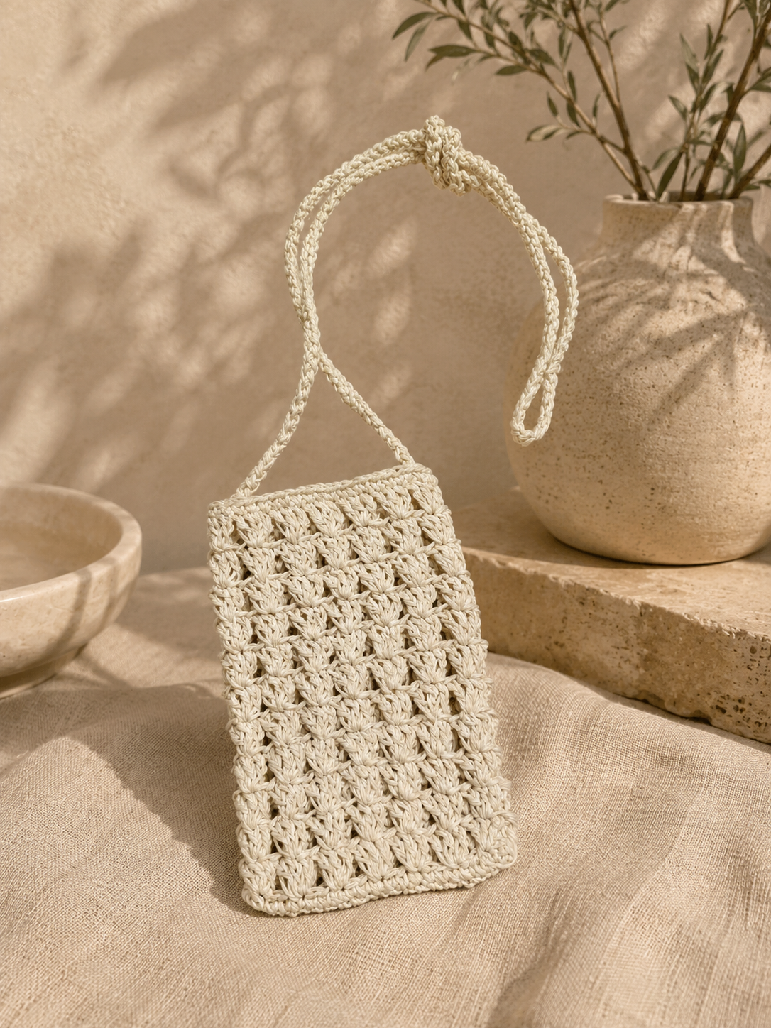 White handmade crochet phone bag displayed in a warm neutral setting.