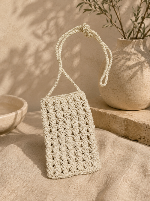 White handmade crochet phone bag displayed in a warm neutral setting.