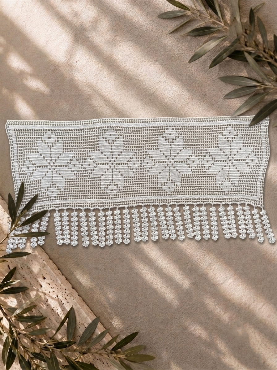 White floral filet crochet lace panel with fringe displayed on neutral fabric