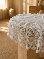 Handmade white round crochet lace table topper draped over a circular table, showing its wide scalloped border.