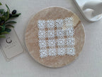 Flat-lay view of a small square white crochet doily showing its symmetrical motif grid and handmade openwork texture.