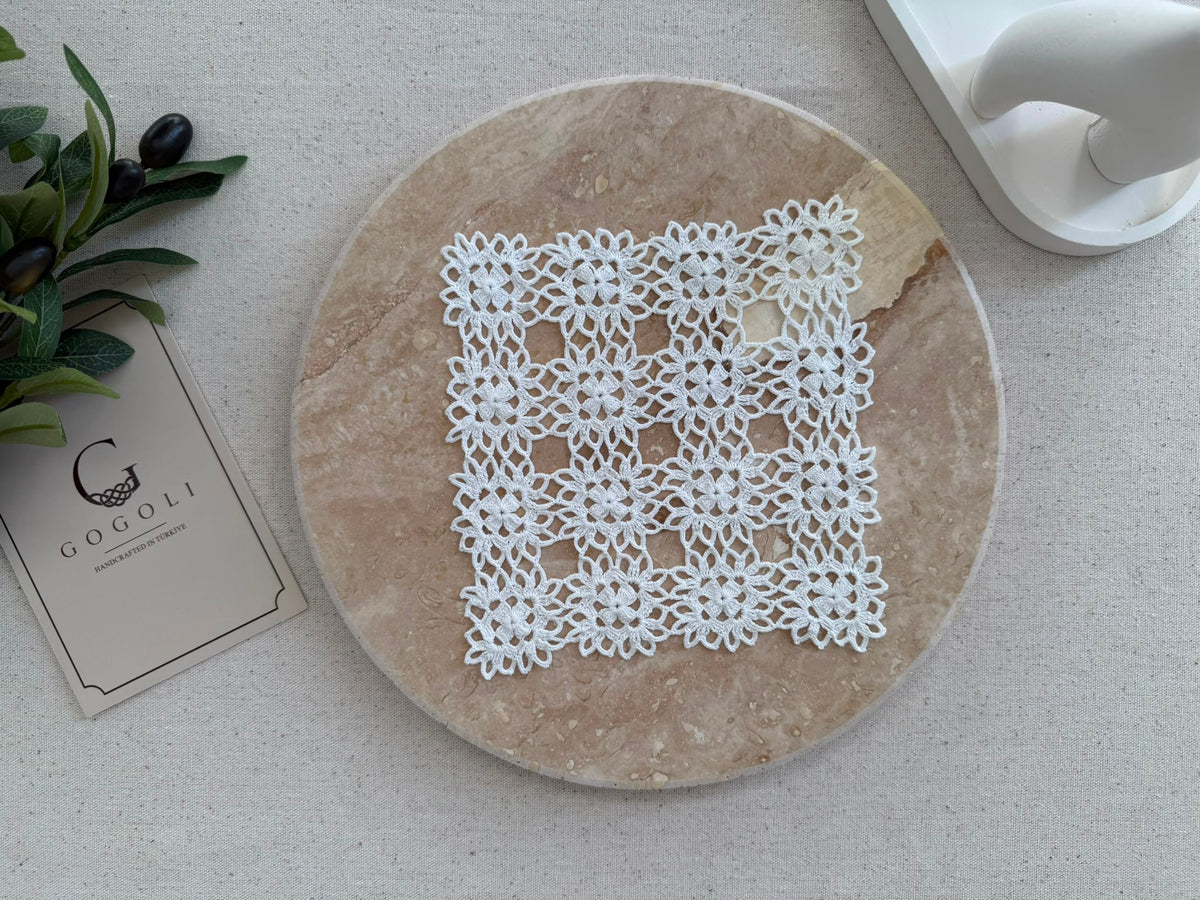 Flat-lay view of a small square white crochet doily showing its symmetrical motif grid and handmade openwork texture.