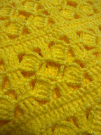 Close-up of the yellow crochet vest showing the strong acrylic yarn, clear stitch definition and textured openwork surface.