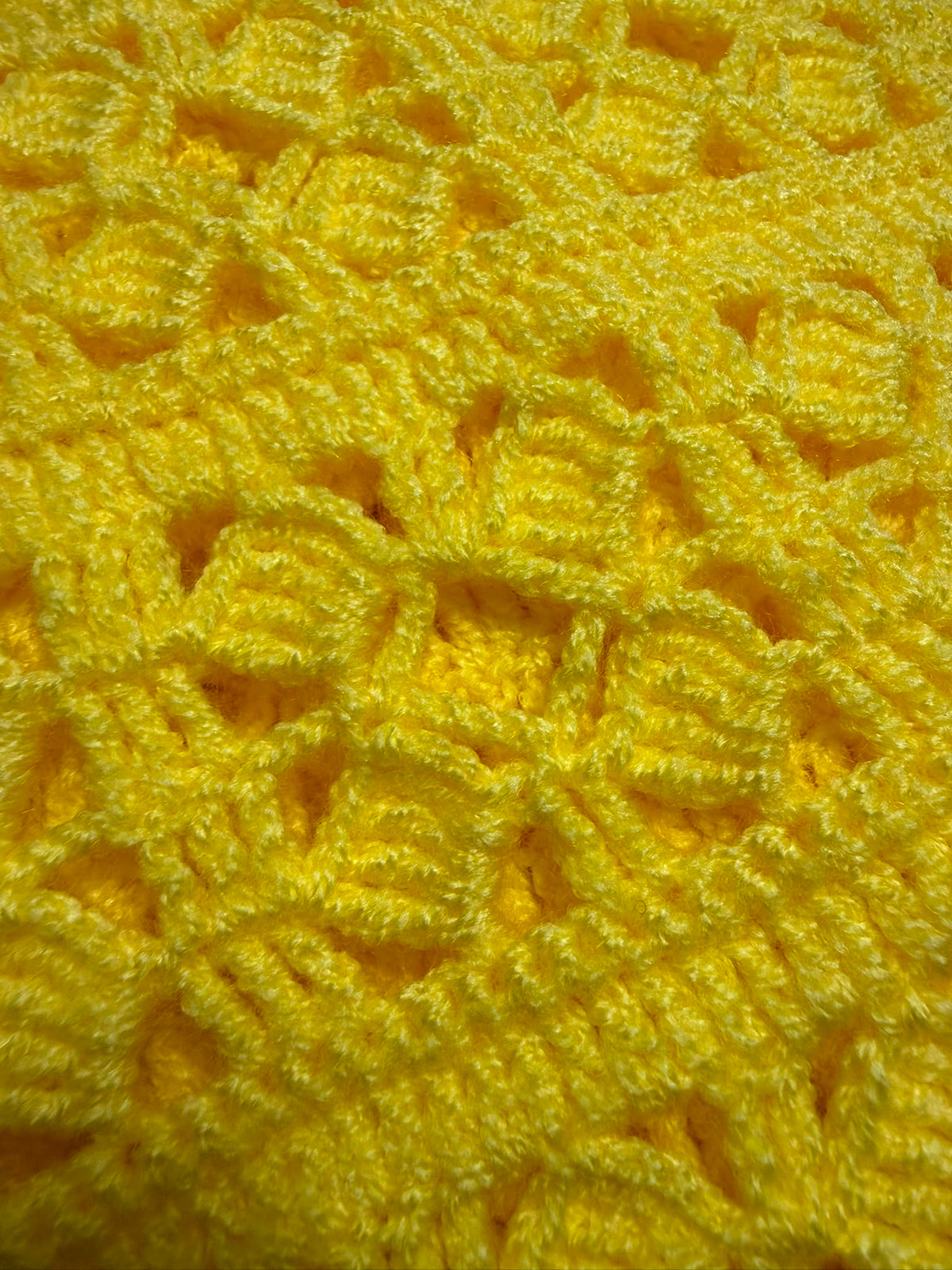 Close-up of the yellow crochet vest showing the strong acrylic yarn, clear stitch definition and textured openwork surface.